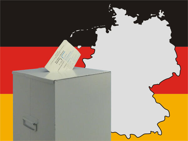 Bild vergrößern: Ein Stimmzettel steckt im Schlitz einer Wahlurne. Im Hintergrund befindet sich der Umriss von Deutschland.