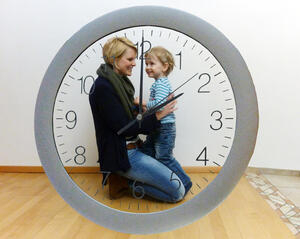 Bild vergrößern: Eine Mutter und ihr Kind befinden sich hinter einer Uhr.