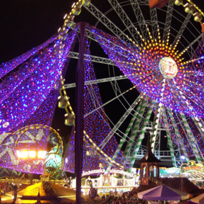 Bild vergrößern: Bunt beleuchtetes Riesenrad vor einem schwarzen Nachthimmel.