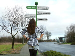 Bild vergrößern: Eine junge Frau steht vor einem Straßenschild, welches in die Richtungen "Ausland" "Universität", "Ausbildung", "Berufskolleg" und "Praktikum" weisen.