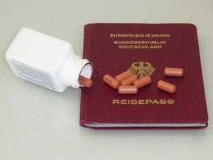 Bild vergrößern: Eine umgekippte Medikamentendose und Tabletten liegen auf einem Reisepass.