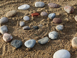 Bild vergrößern: Aus Steinen gelegte Spirale auf Sand.