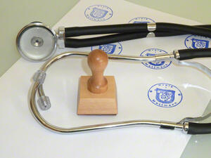 Bild vergrößern: Ein Stethoskop und ein Stempel liegen auf einem gestempelten Papier.