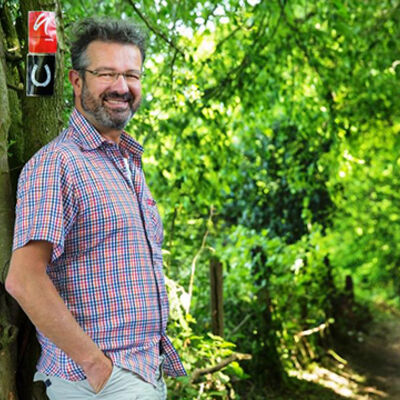 Bild vergrößern: Manuel Andrack posiert auf einem Feldweg vor dem Hinweisschild "neandelrlandsteig".