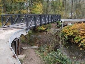 Bild vergrößern: Brücke über einem Bach in einem Waldgebiet.