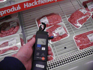Bild vergrößern: Ein Lebensmittelthermometer misst die Temperatur eines in einer Kühltheke befindlichen Packung Hackfleisch.