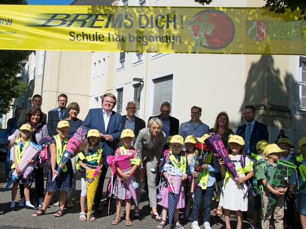 Die NRW-Schulministerin  Dorothee Feller steht zwischen Schulanfängern der Grundschule Anne Frank in Ratingen unter dem Banner "Brems dich! Schule hat begonnen". Im Hintergrund die Schulleitung, Funktionäre und Eltern.