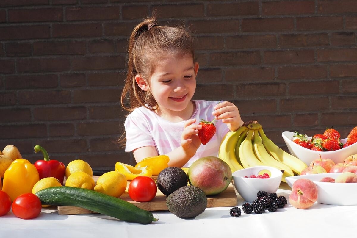 Bild vergrößern: Ein Kind sitzt an einem Tisch und erkundet verschiedene Obst- und Gemüsesorten.