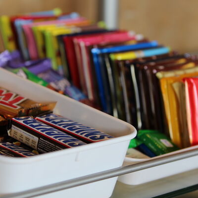Bild vergrößern: Verschiedenartige Süßigkeiten liegen nebeneinander gereiht in einer Auslage.